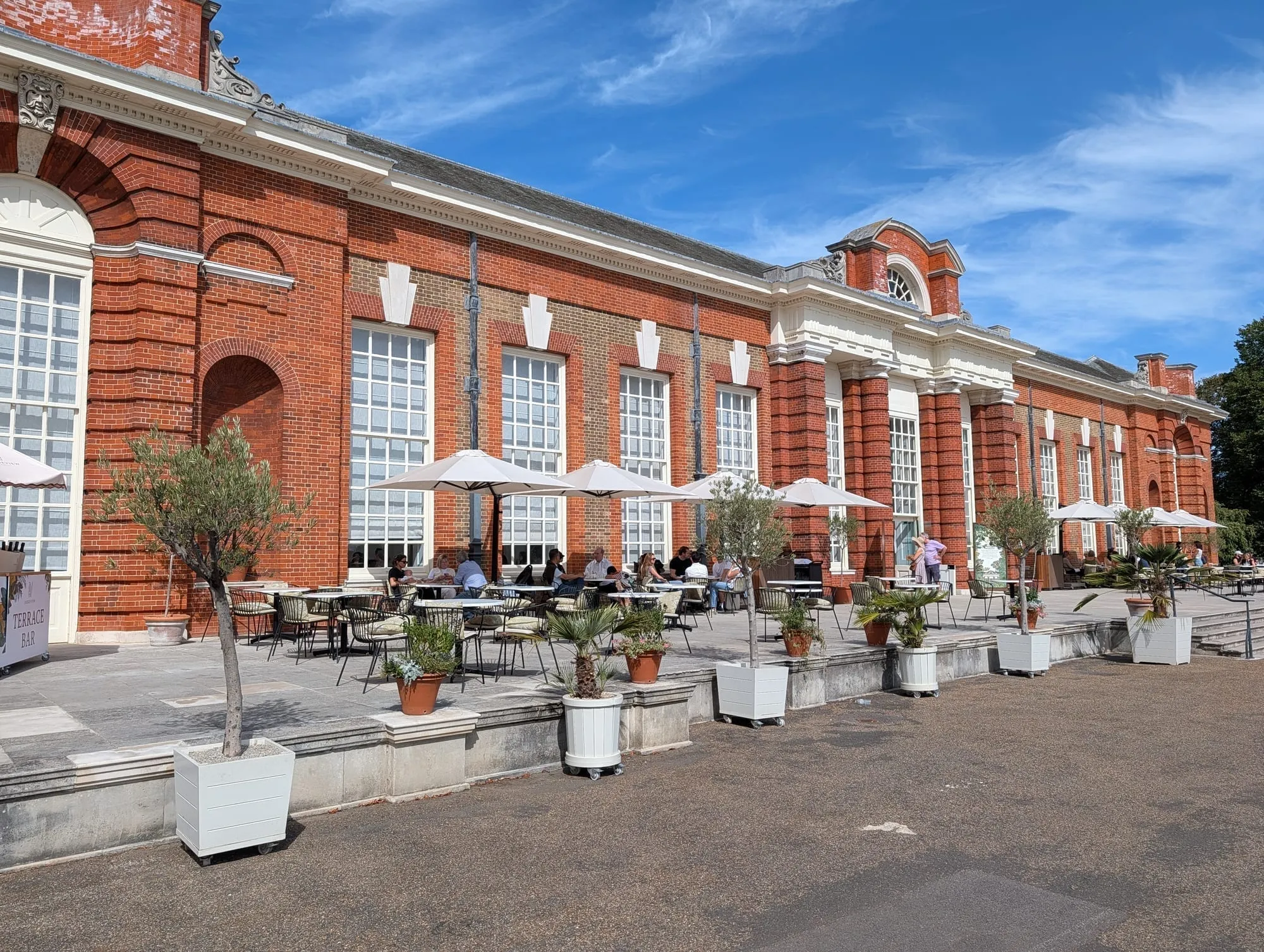 The Pavilion cafe at Kensington Palace, a long red brick building with outdoor tables under white umbrellas