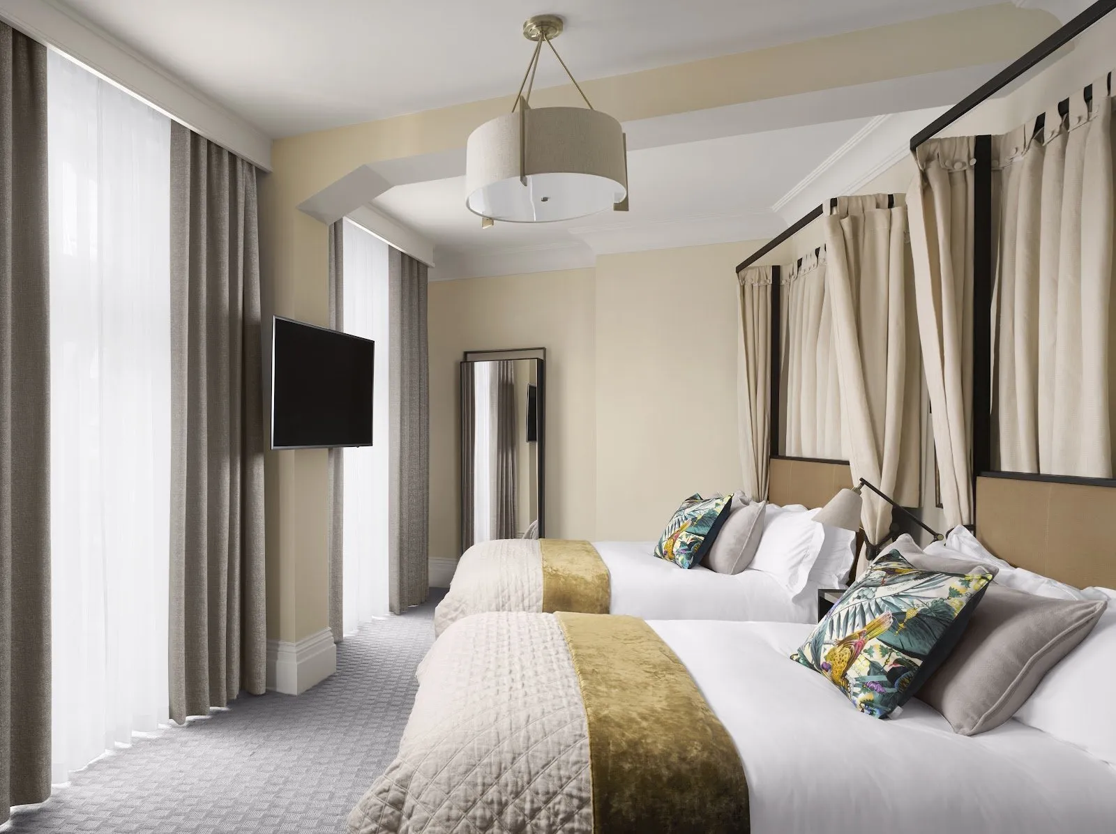 A twin room at Kimpton Fitzroy London with a four-poster-style bed frame, gold accents and heavy curtains drawn back from the beds