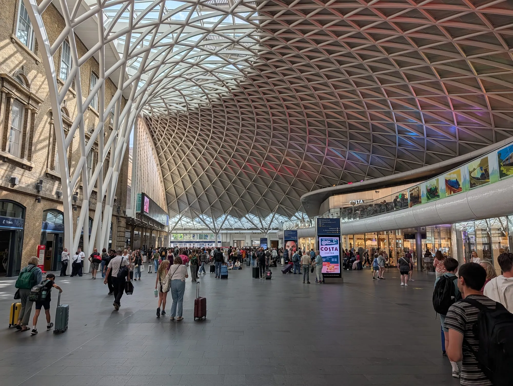 The white lattice roof of the Western Concourse at King's Cross station fanning out above the crowds