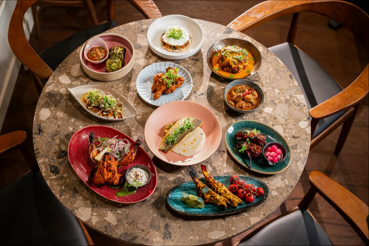 A round marble table at Kokum filled with coastal Indian dishes, whole grilled fish, tandoori meats and curries