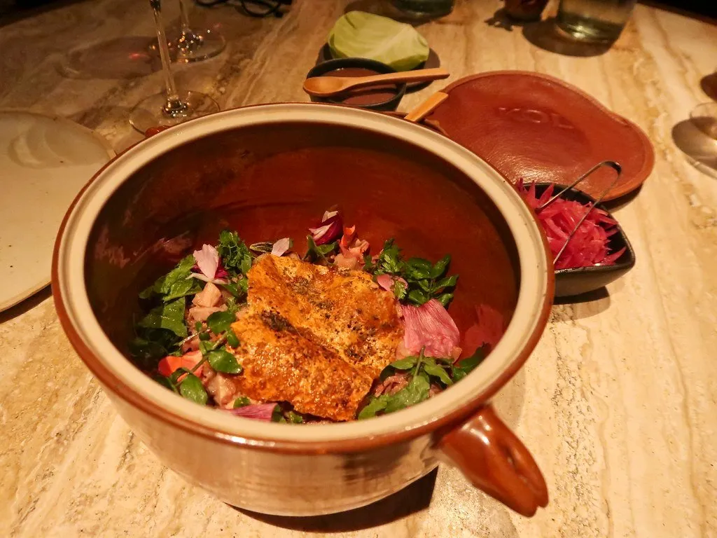 A clay bowl of shredded meat with herbs and pickled onion