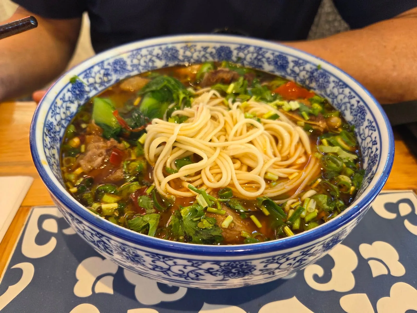 A large bowl of beef noodle soup with hand-pulled noodles, herbs and chopped spring onion