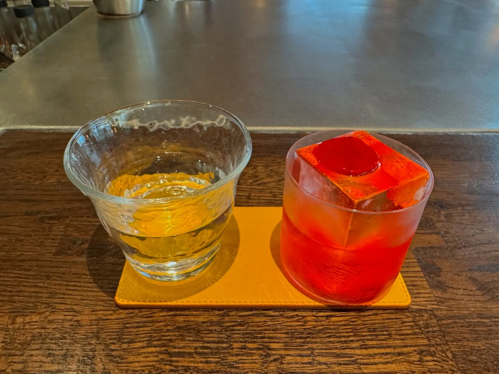 Two cocktails on yellow coasters on a wood bar