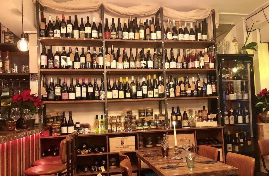 Shelves of wine bottles reaching to the ceiling behind the counter at Lady of the Grapes, with jars and preserves below and a candlelit table in front