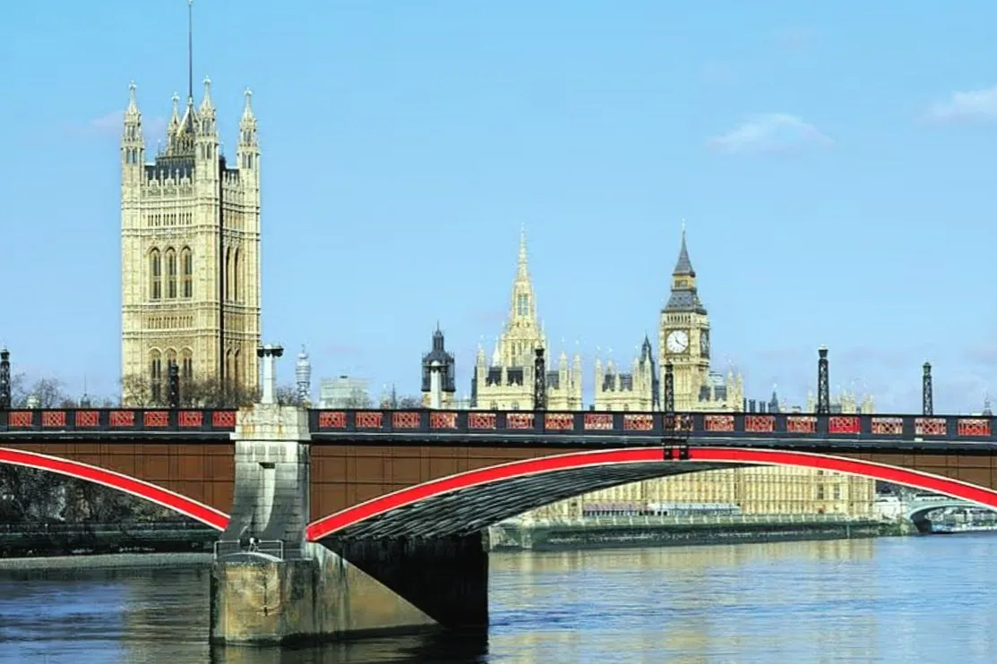 Lambeth Bridge's red-painted arches and parapet over the Thames, with the Victoria Tower and the Elizabeth Tower of the Houses of Parliament behind