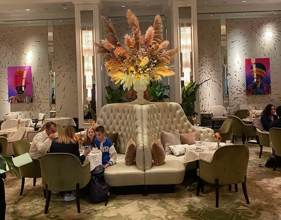 The Palm Court at the Langham, with a tall dried-flower arrangement above a curved buttoned banquette and green armchairs