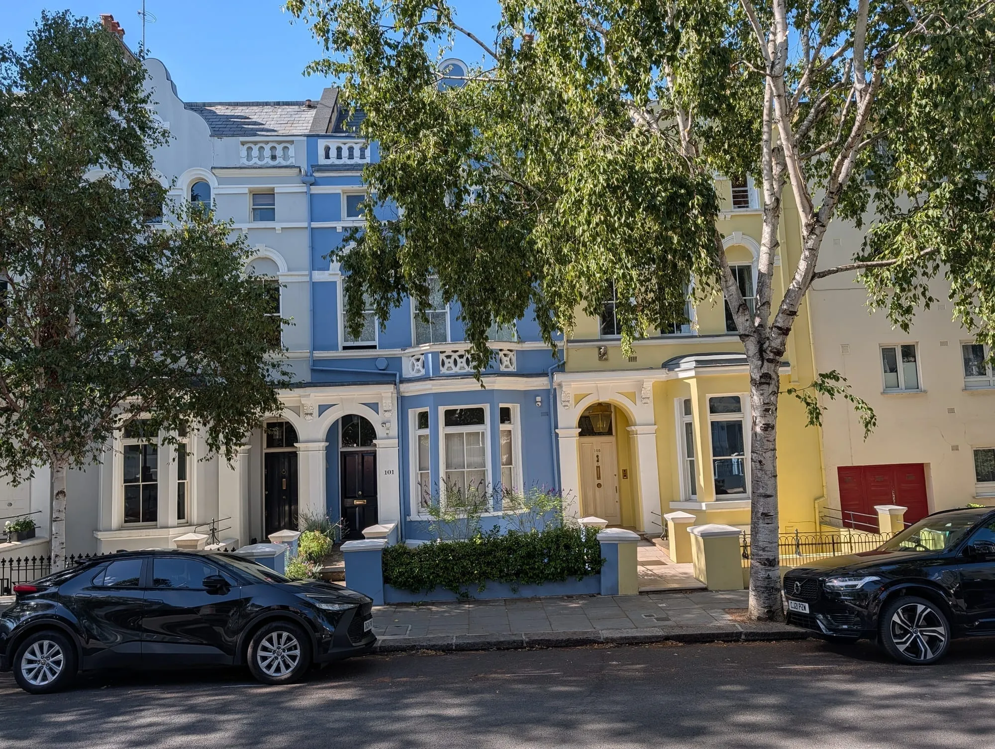 Large stucco houses on Lansdowne Road painted in pale yellow, cream and soft blue behind mature street trees
