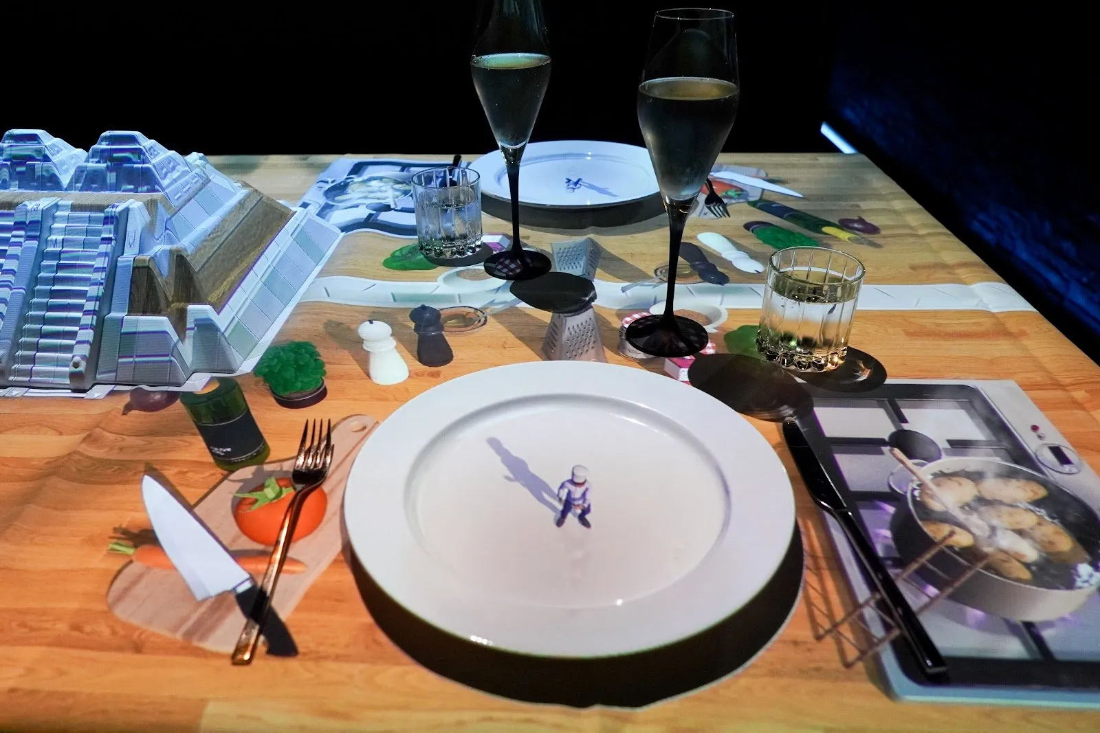 A tiny animated chef projected onto a dinner plate, among projected kitchen tools on the table