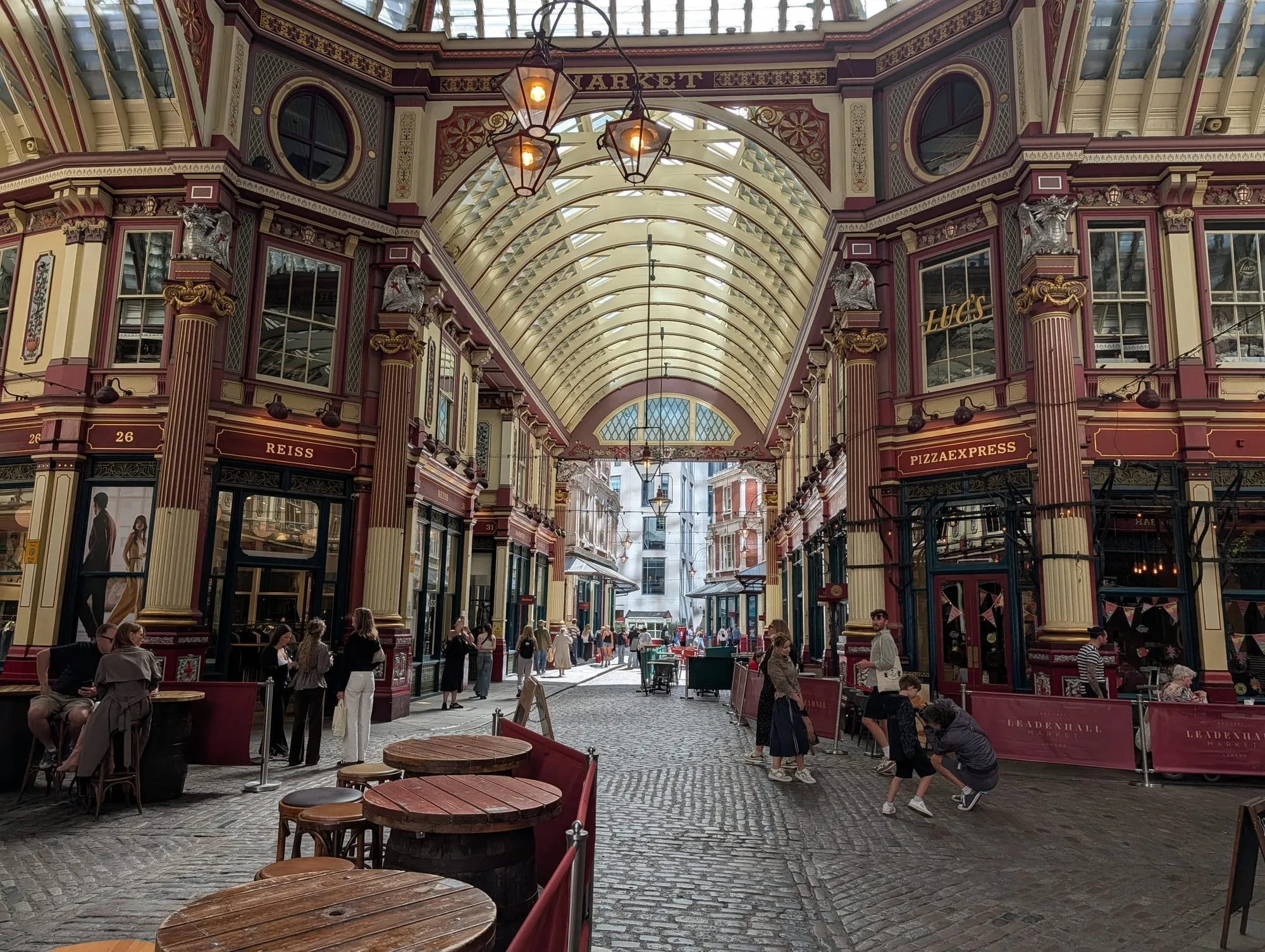 The cream, maroon and green painted ironwork of Leadenhall Market's arcade under its glass roof, with shopfronts and lanterns down both sides