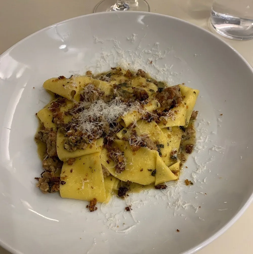 Wide ribbons of fresh egg pasta with sausage ragu, crisp breadcrumbs and grated cheese in a shallow bowl