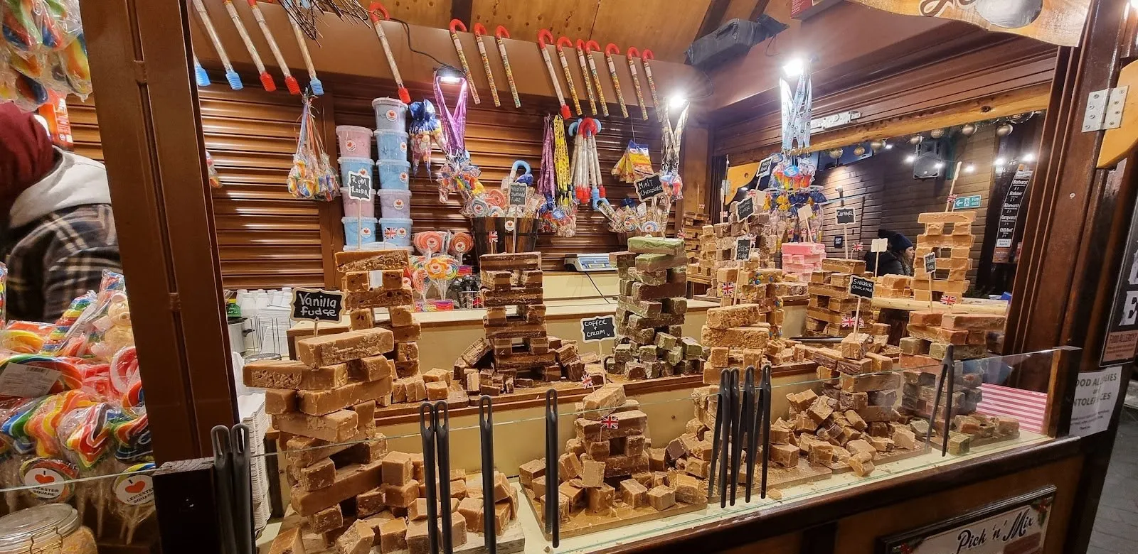 A wooden chalet counter stacked with towers of fudge labelled vanilla, mint chocolate and coffee and cream, with lollipops, candy floss tubs and "I love Leicester Square" lollies around it