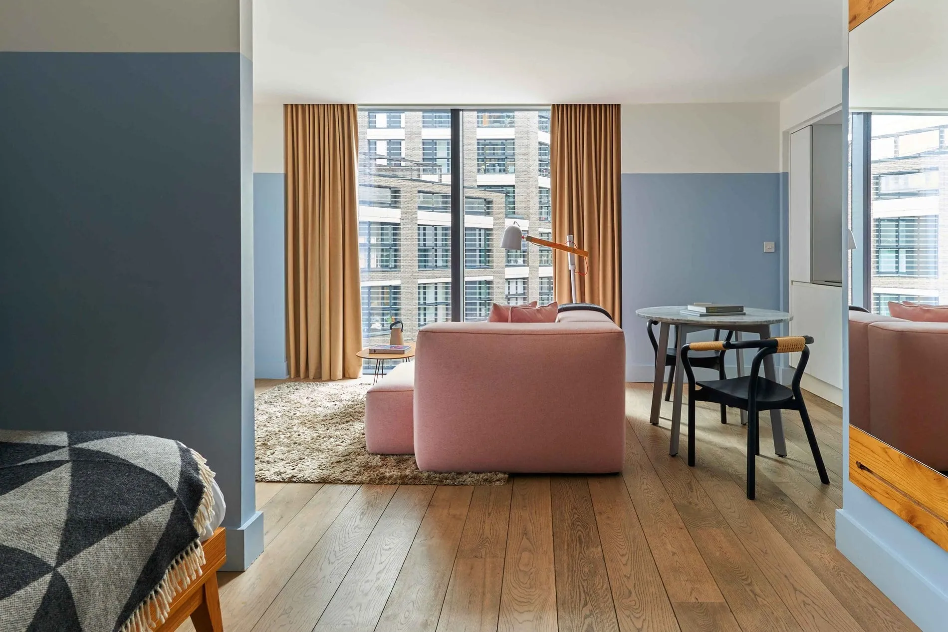 The living area of a studio at Leman Locke, with a pink sofa, a round marble dining table and floor-to-ceiling windows