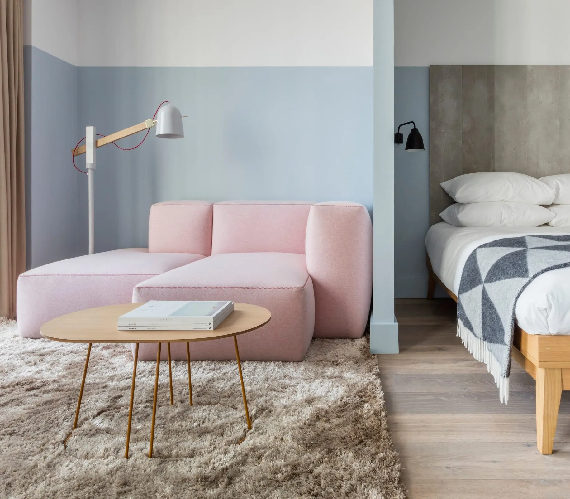 A room at Leman Locke with a pink modular sofa and a bed with a grey headboard, visible through an open partition