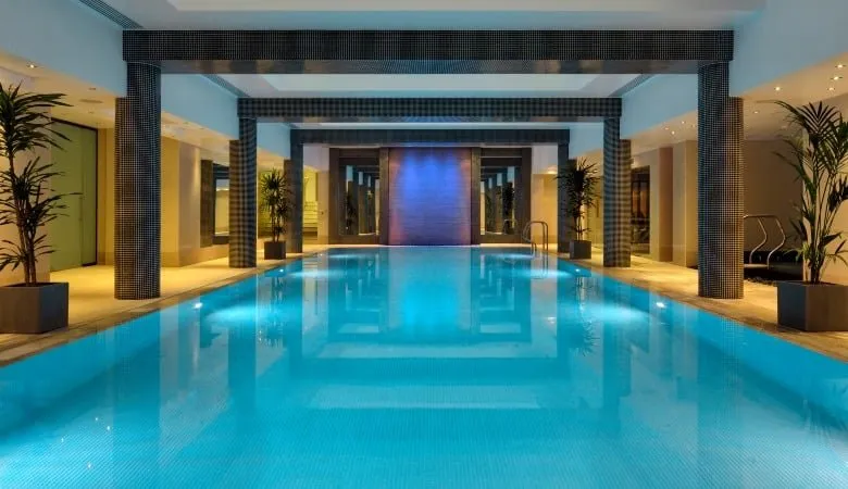 The indoor pool at Leonardo Royal London St Paul's, with tiled columns along both sides and palms in planters