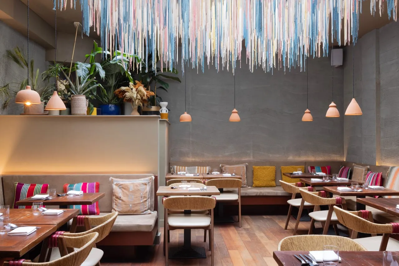 A Peruvian dining room hung with a dense ceiling installation of pink, blue and cream threads, with terracotta pendant lamps and woven rattan chairs below