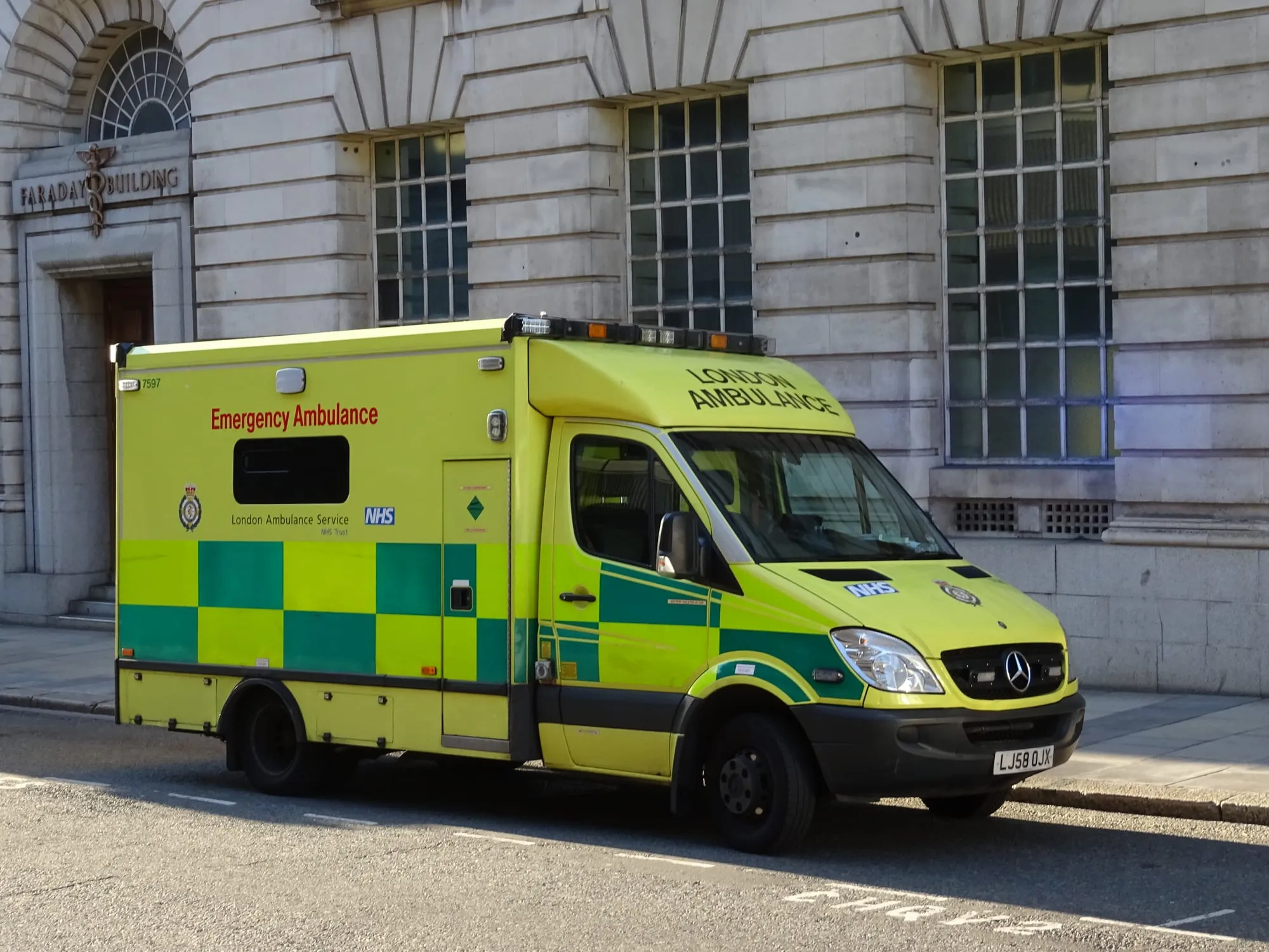 A yellow and green London Ambulance Service NHS emergency ambulance parked outside a stone-fronted City of London building