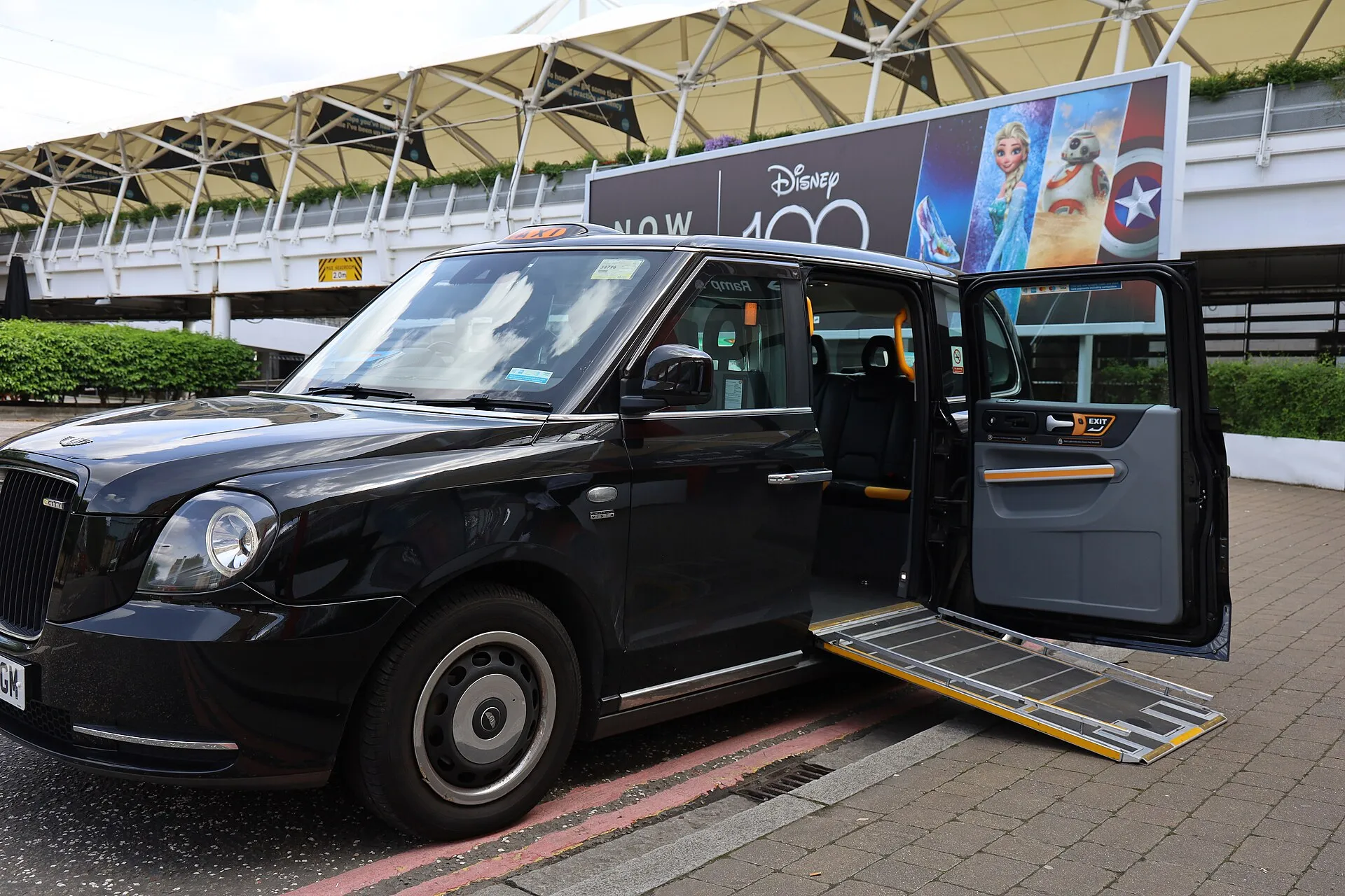 A London black cab at the kerb with its wheelchair ramp folded out from the passenger door onto the pavement