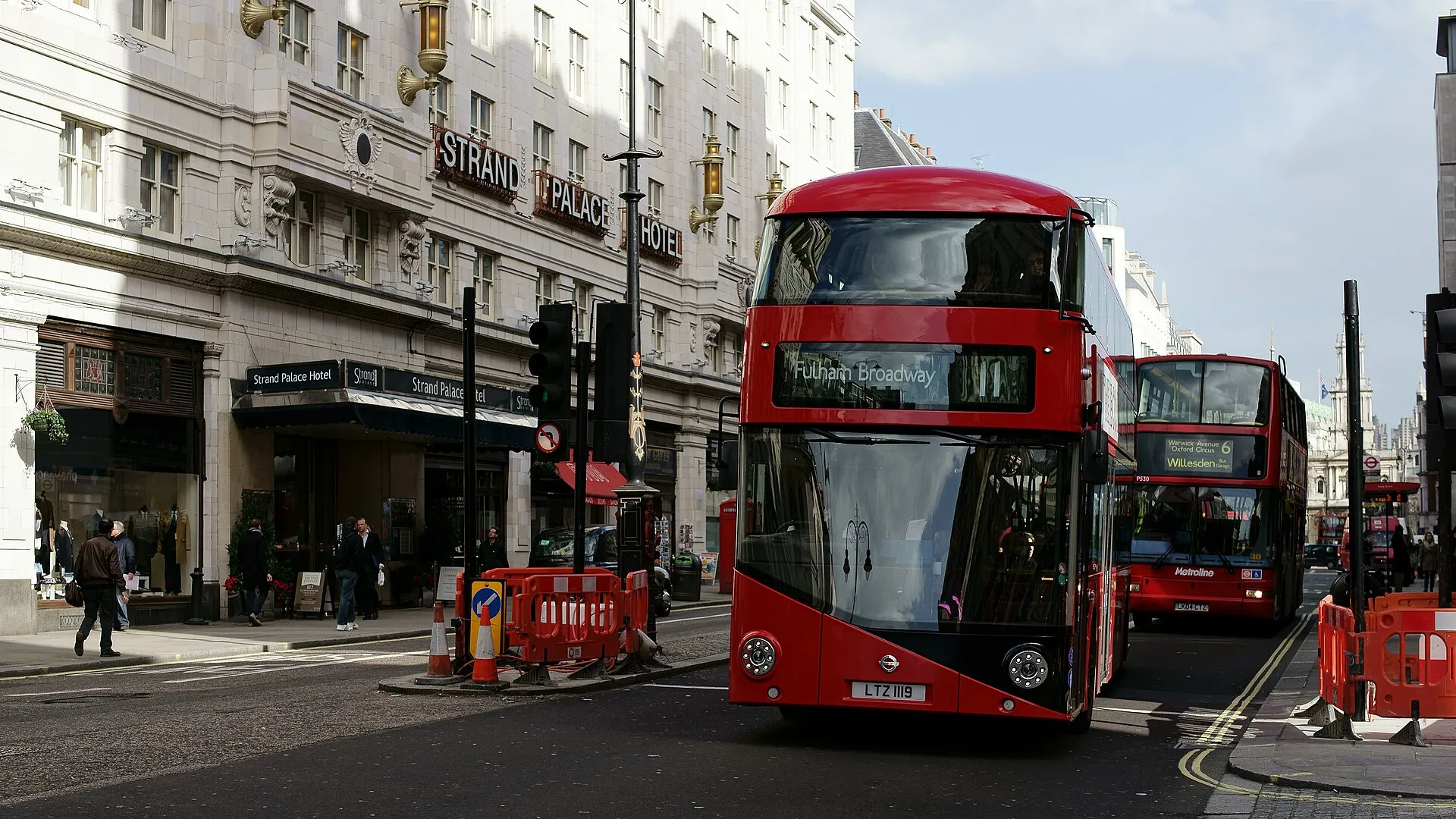 A red New Routemaster double-decker bus travelling through central London