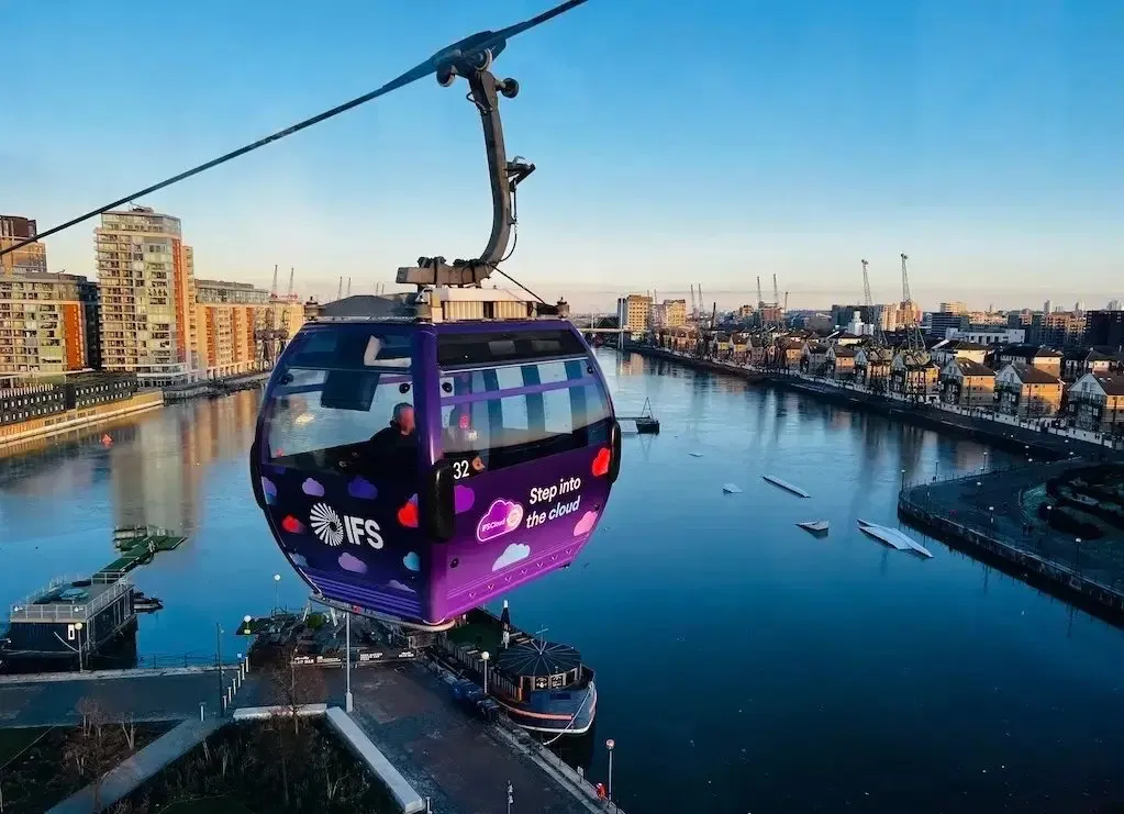 An IFS Cloud Cable Car cabin crossing the Royal Docks at dusk, with the Thames and the Docklands skyline behind