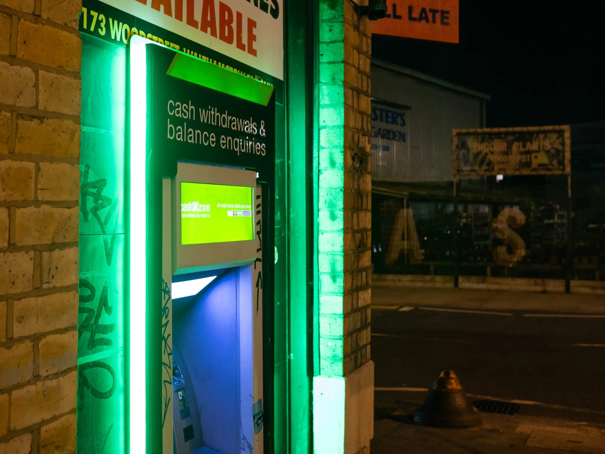 An illuminated independent Cashzone cash machine advertising cash withdrawals and balance enquiries, set into a brick wall on a London street at night