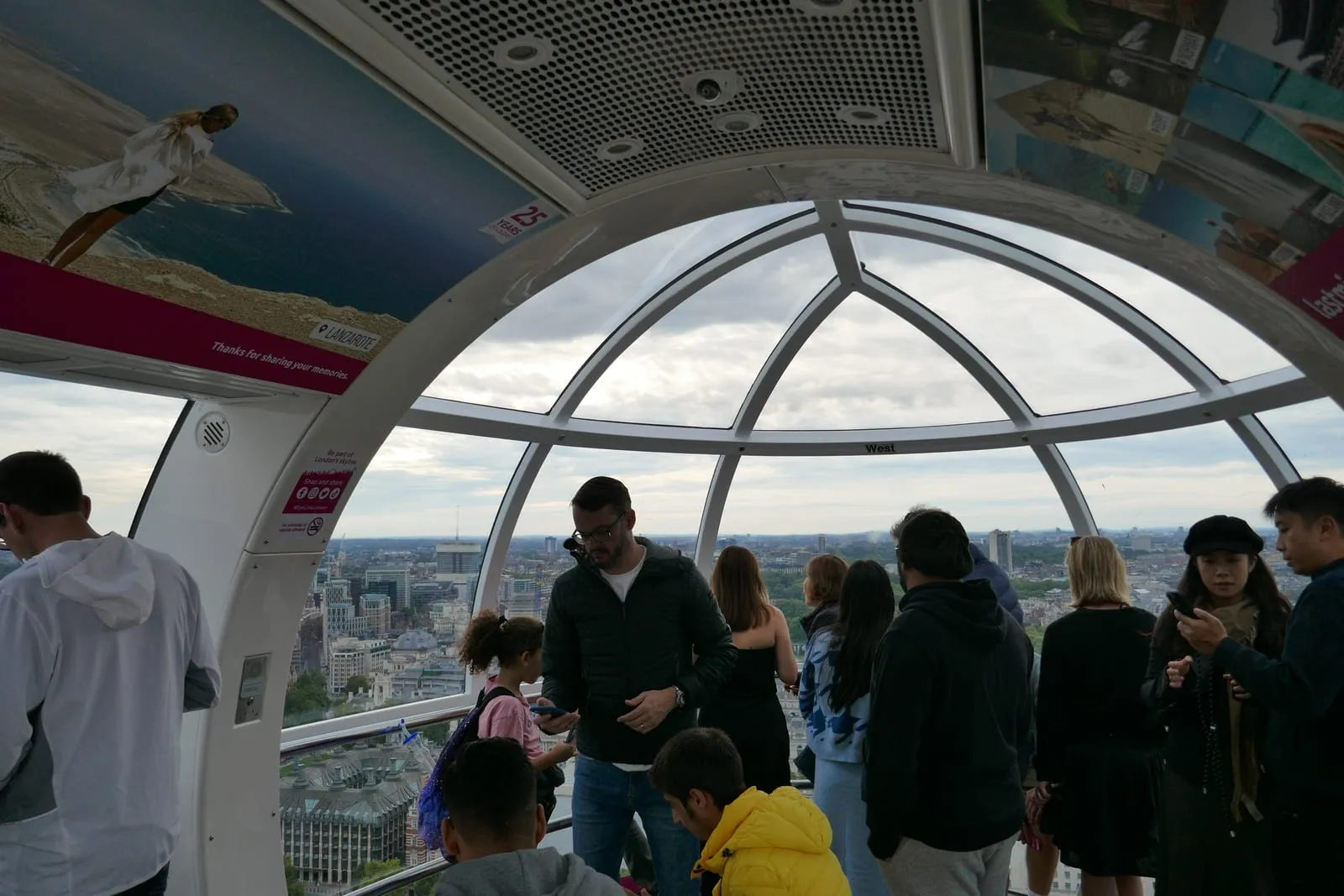Passengers standing inside an air-conditioned glass capsule on the London Eye looking towards the River Thames
