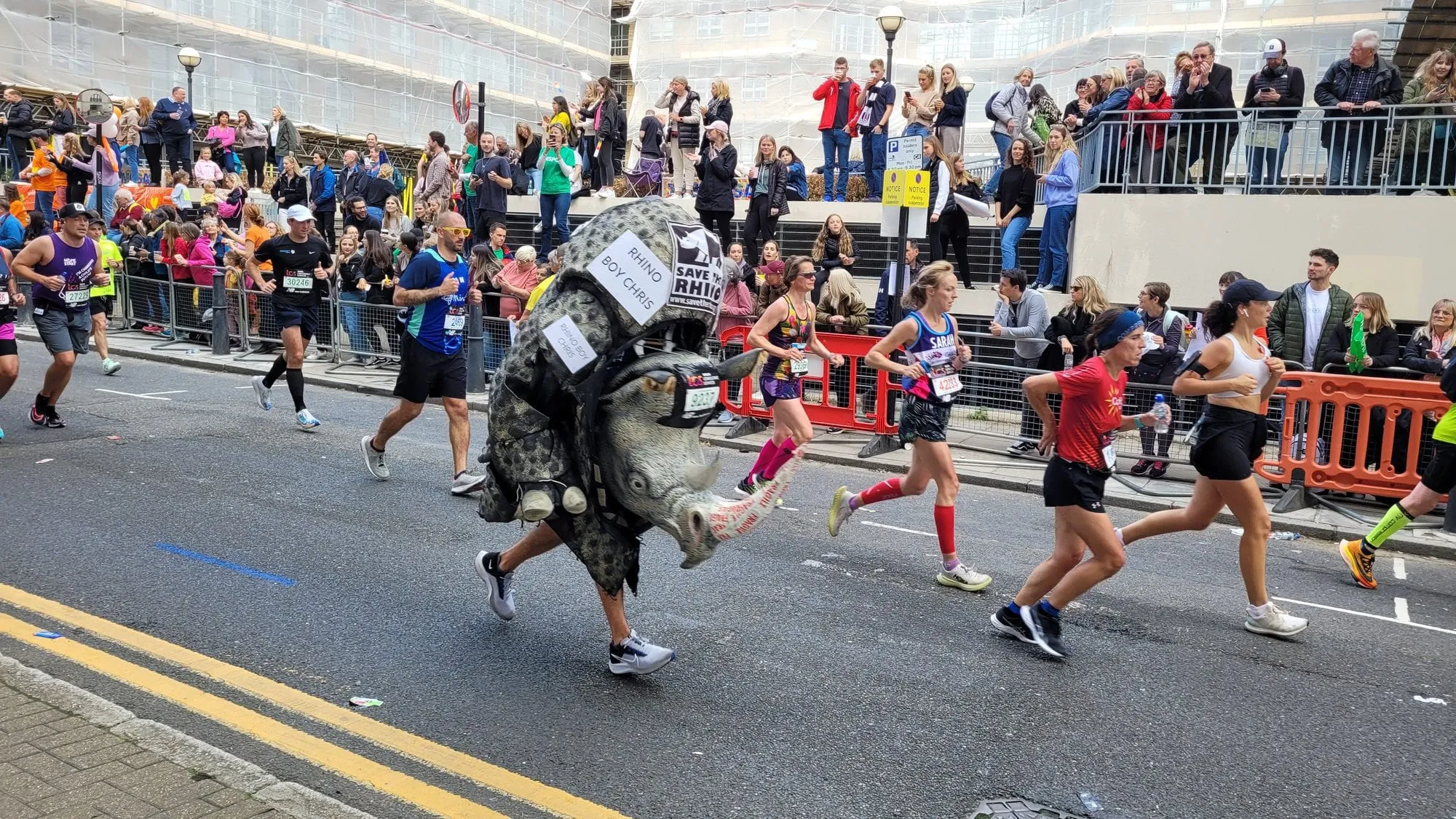 A runner in a full rhino costume on the London Marathon course, with spectators packed along the barriers on both sides