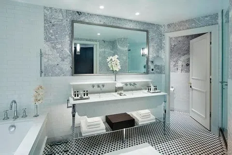 A bathroom at the London Marriott County Hall with a bath, twin basins on a chrome stand, wallpaper printed with a map of London and a black-and-white mosaic floor