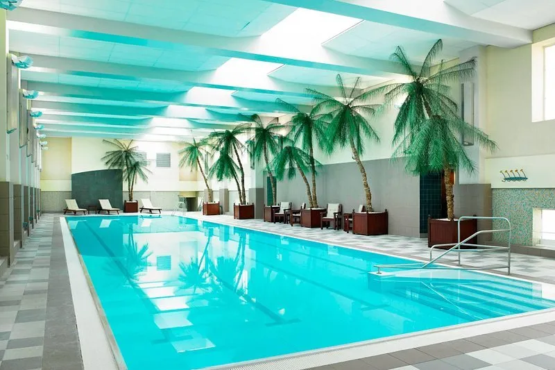 The 25-metre indoor swimming pool at London Marriott Hotel County Hall with loungers, palms and a glass roof