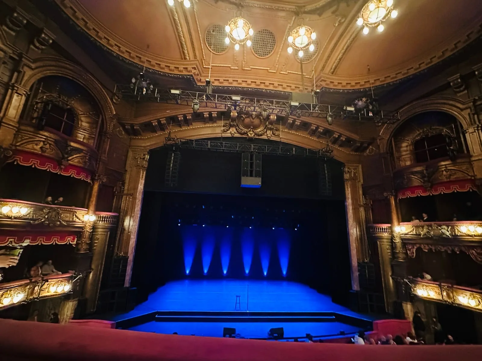 The London Palladium's gilded proscenium arch and stage boxes, lit by chandeliers, with a bare stage in blue light
