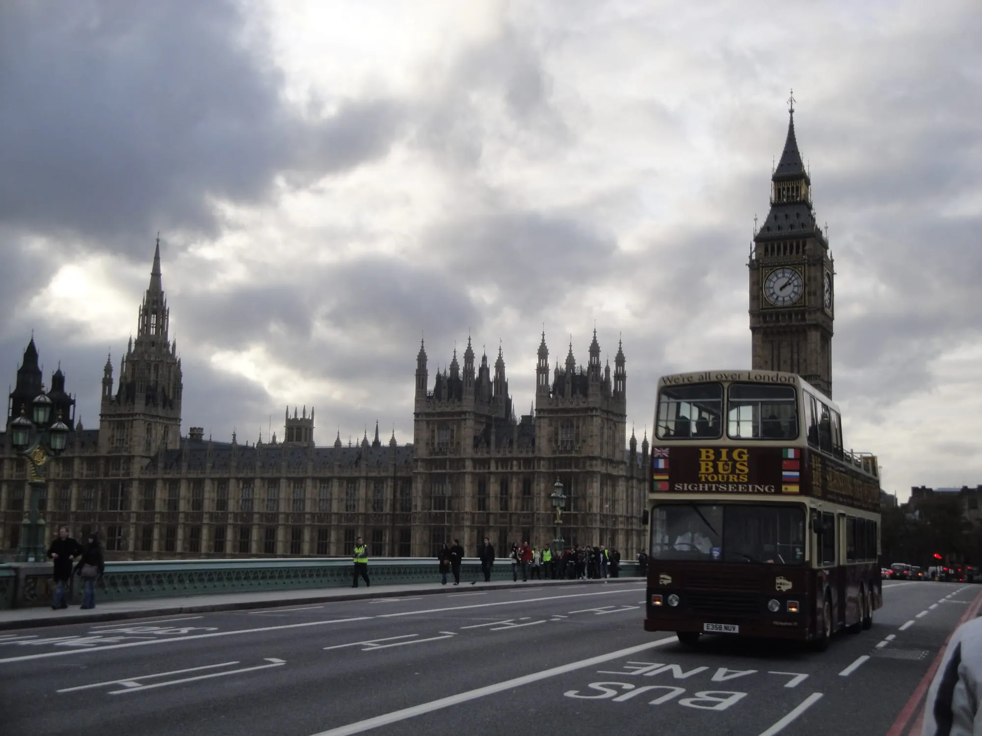 An open-top red sightseeing tour bus passing the Palace of Westminster