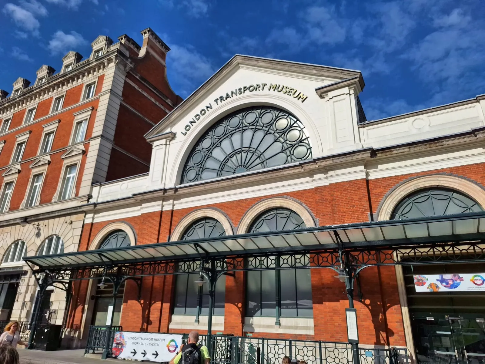 The London Transport Museum's glass-arched Victorian market building on Covent Garden Piazza, under a blue sky