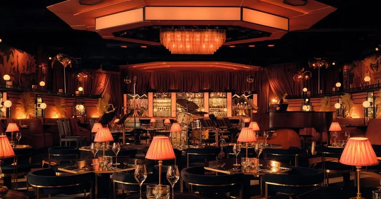 The 58th Street room set as a supper club, with a grand piano and drum kit on a low stage, pink shaded table lamps on every table and a lit sign reading 58th Street Country Club behind the bar