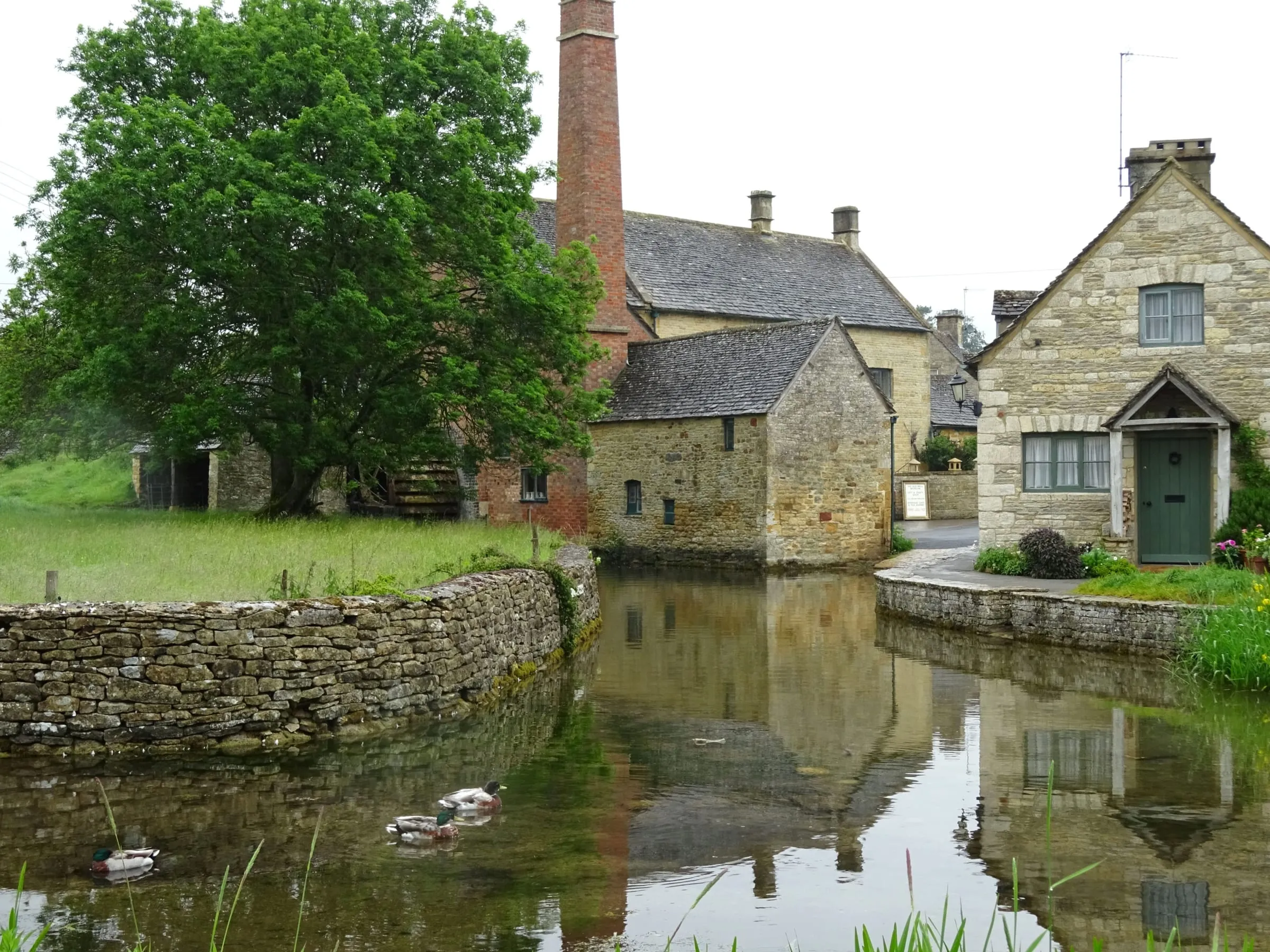 The old mill and cottages reflected in the millpond at Lower Slaughter, ducks on the water