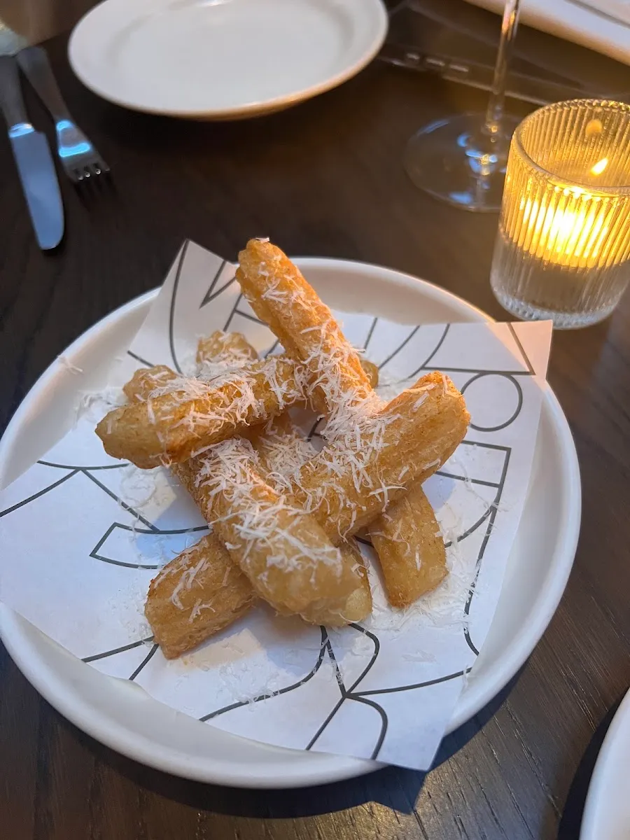 Crisp parmesan fries piled on paper and dusted with grated cheese, on a white plate
