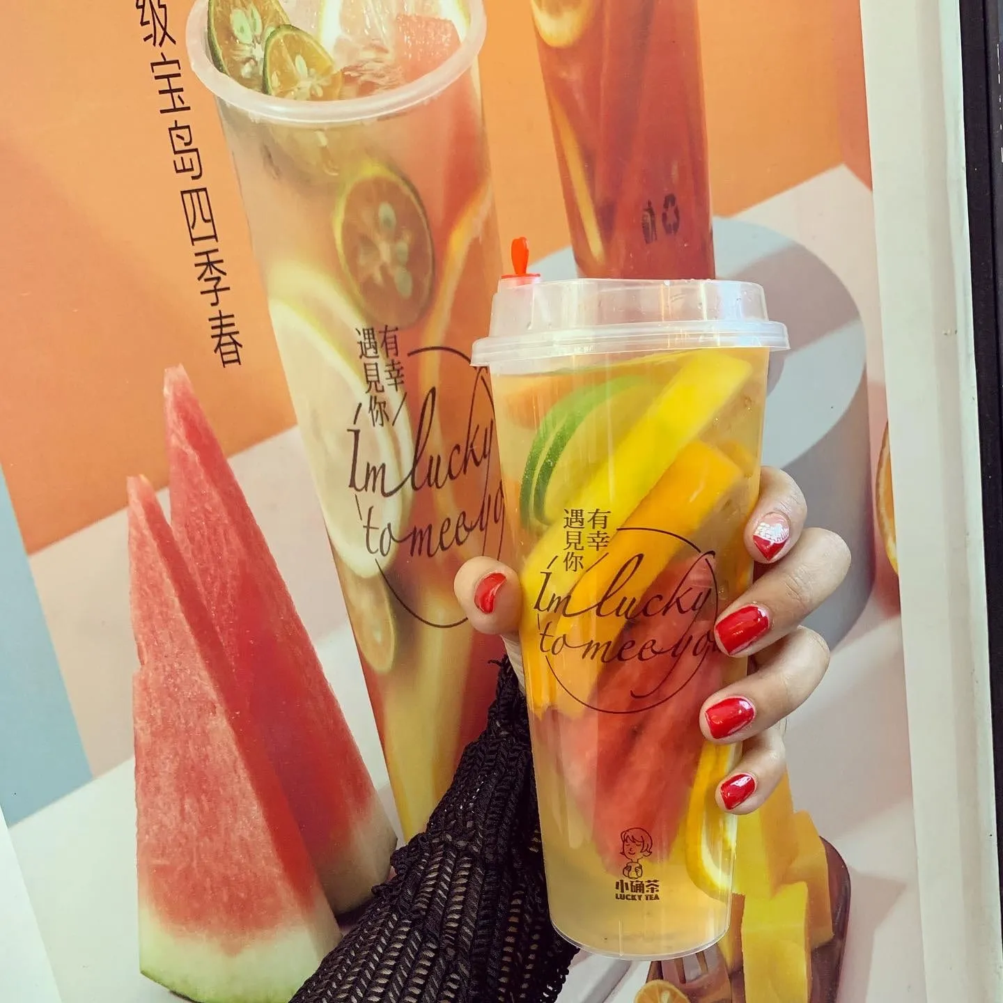 A Lucky Tea fruit tea packed with slices of watermelon, lime and orange, held up against a poster of the same drink