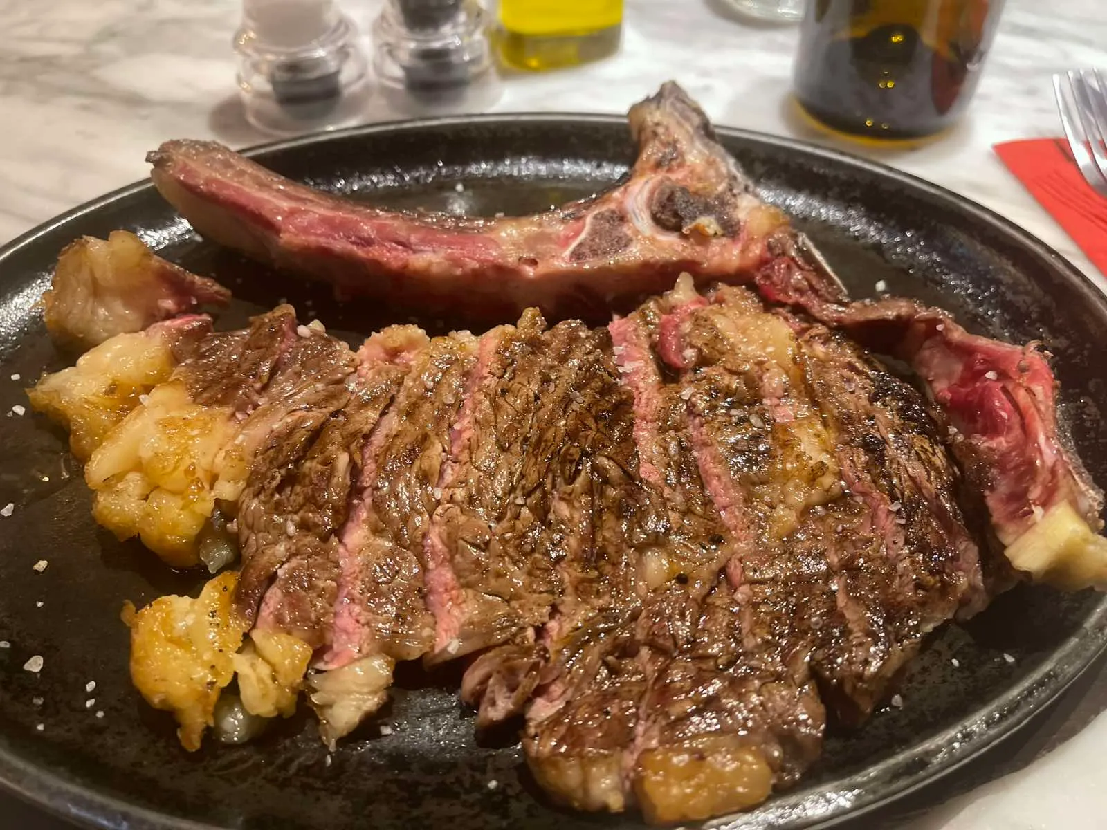 Sliced tagliata steak with the bone alongside, seared and pink in the middle, on a dark plate with sea salt