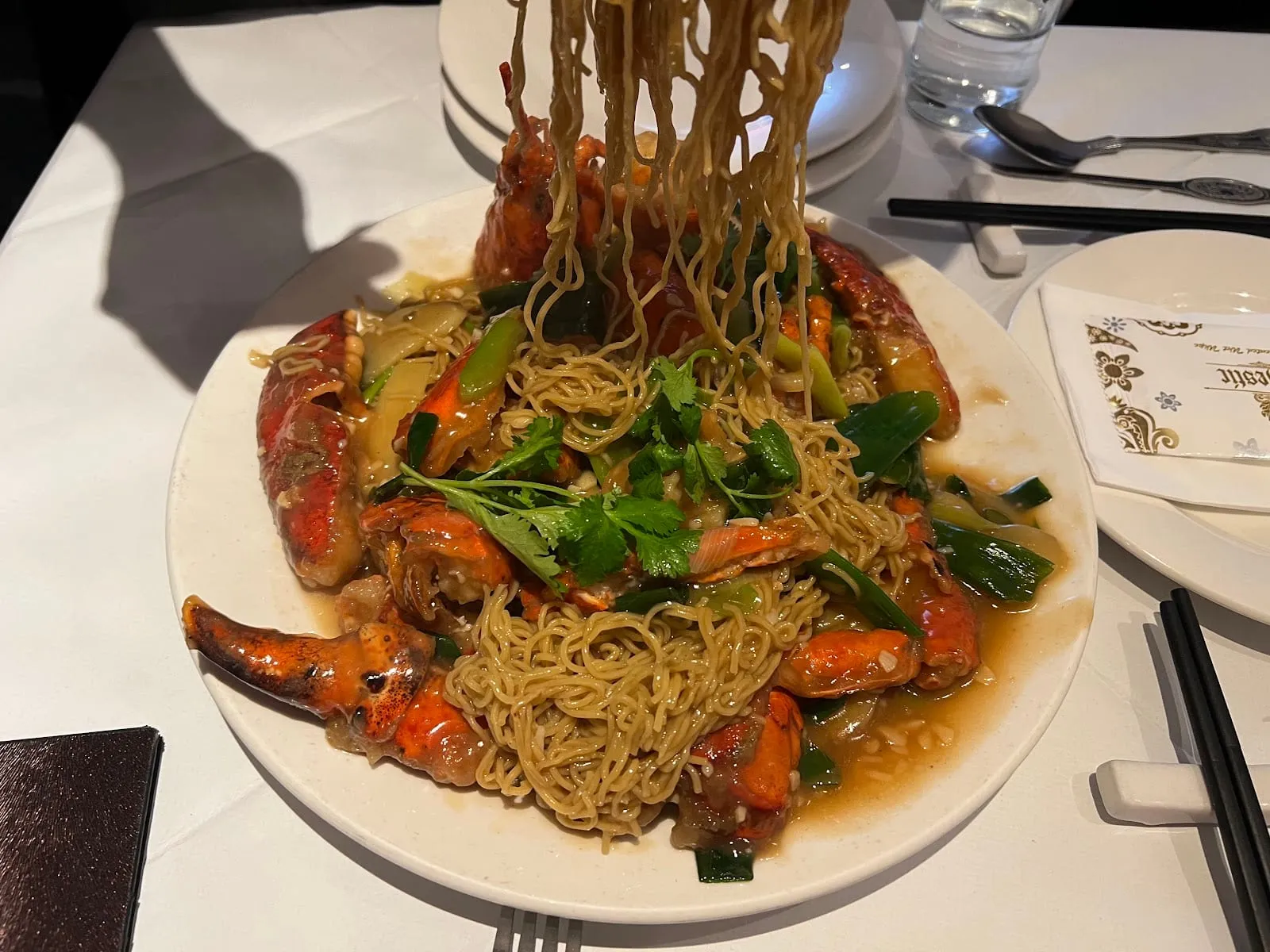 A whole lobster in its shell piled with noodles, spring onion and coriander, on a white plate
