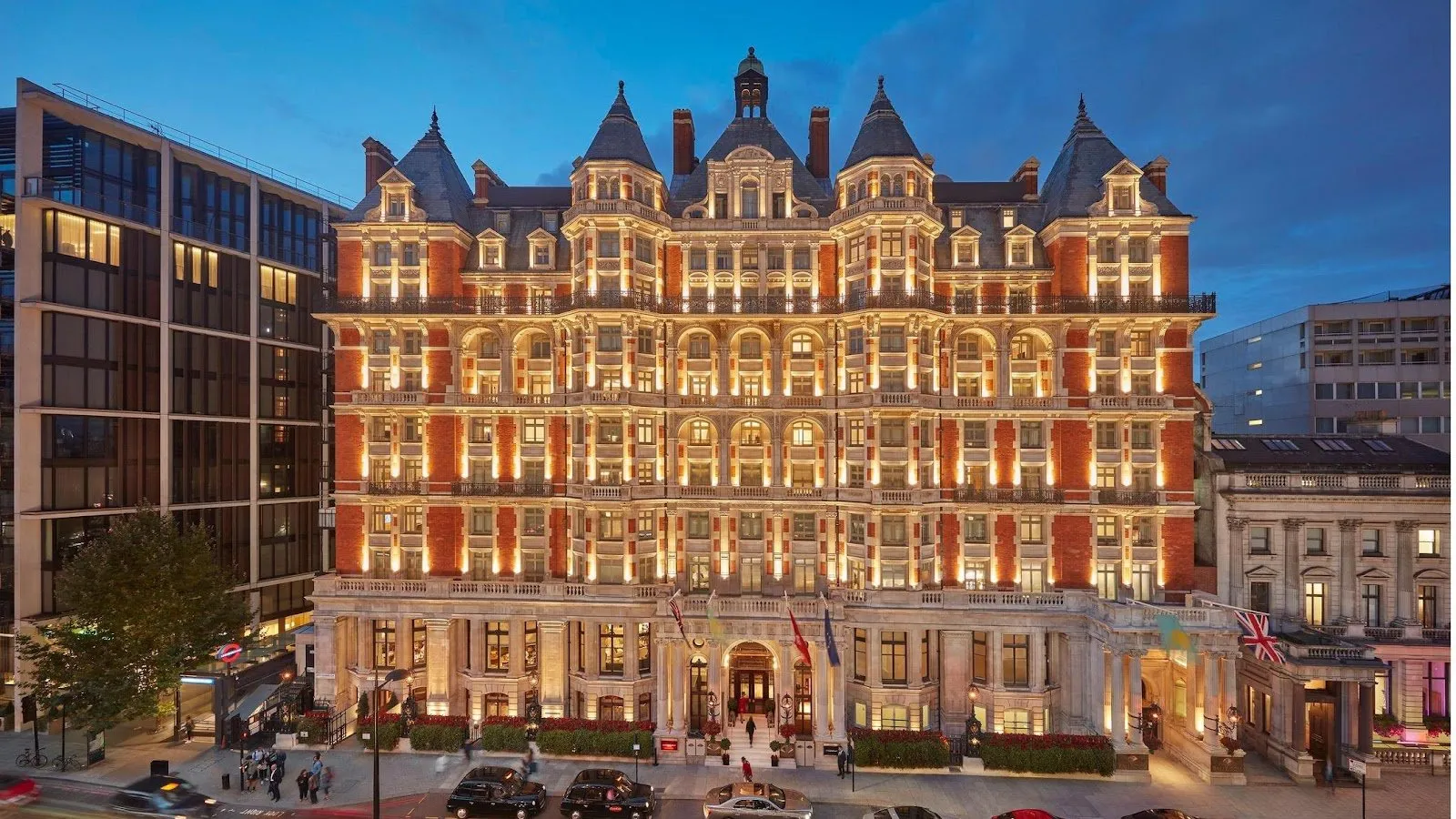 Mandarin Oriental Hyde Park's red-brick Victorian facade lit up at dusk, with Union Flags flying over Knightsbridge and black cabs passing