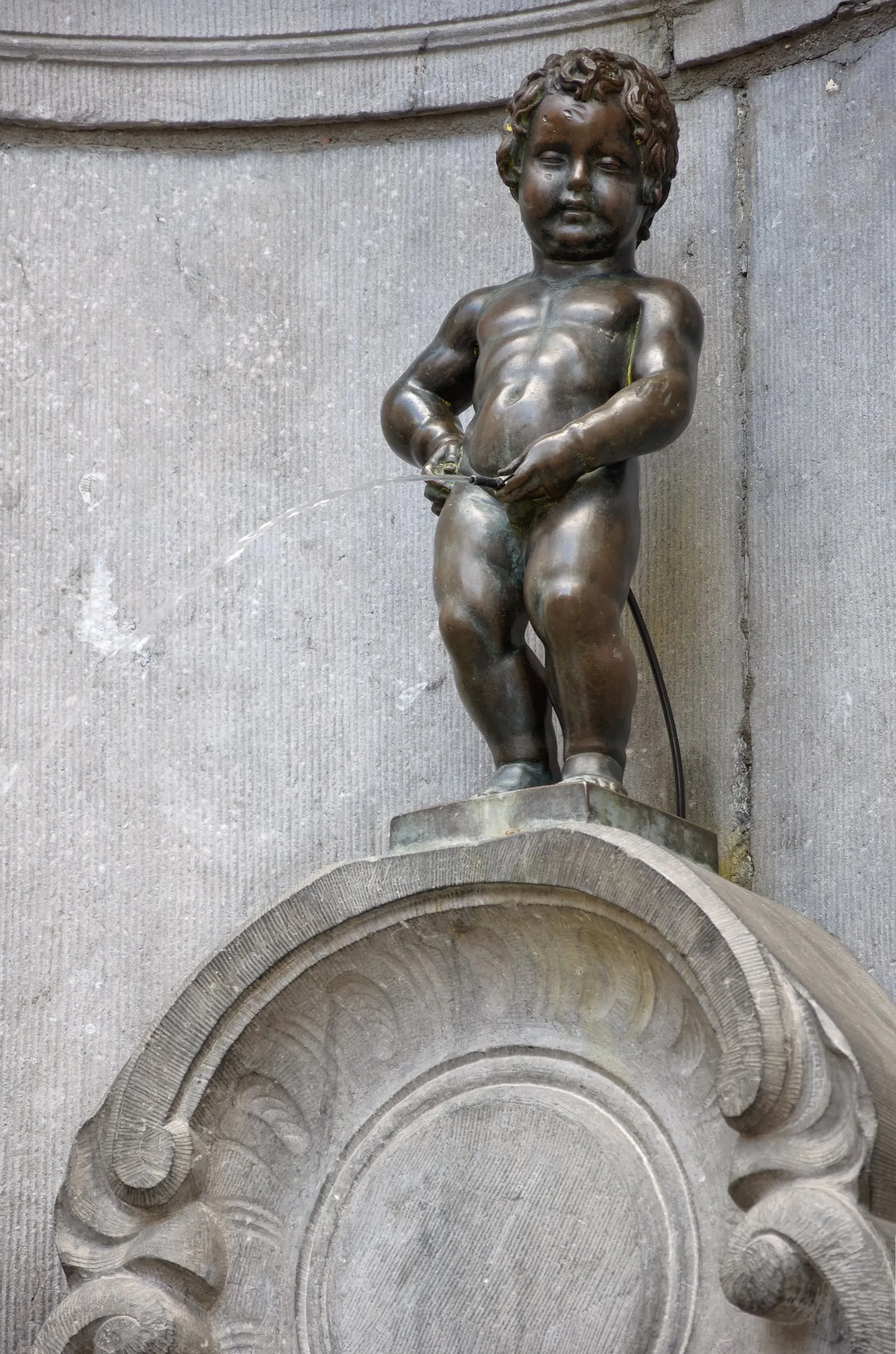Manneken Pis, the bronze fountain figure in its stone niche, a thin arc of water running from the statue