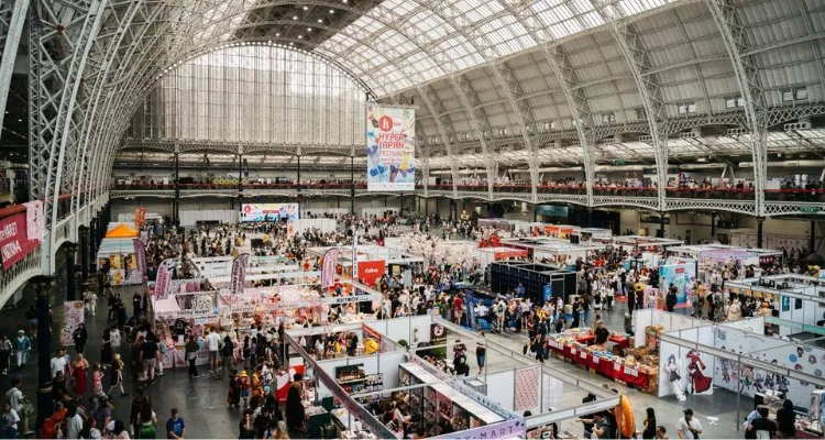 An aerial view of Olympia's Grand Hall packed with HYPER JAPAN Festival market stalls under the glass roof, with the event's banner hanging above the crowd