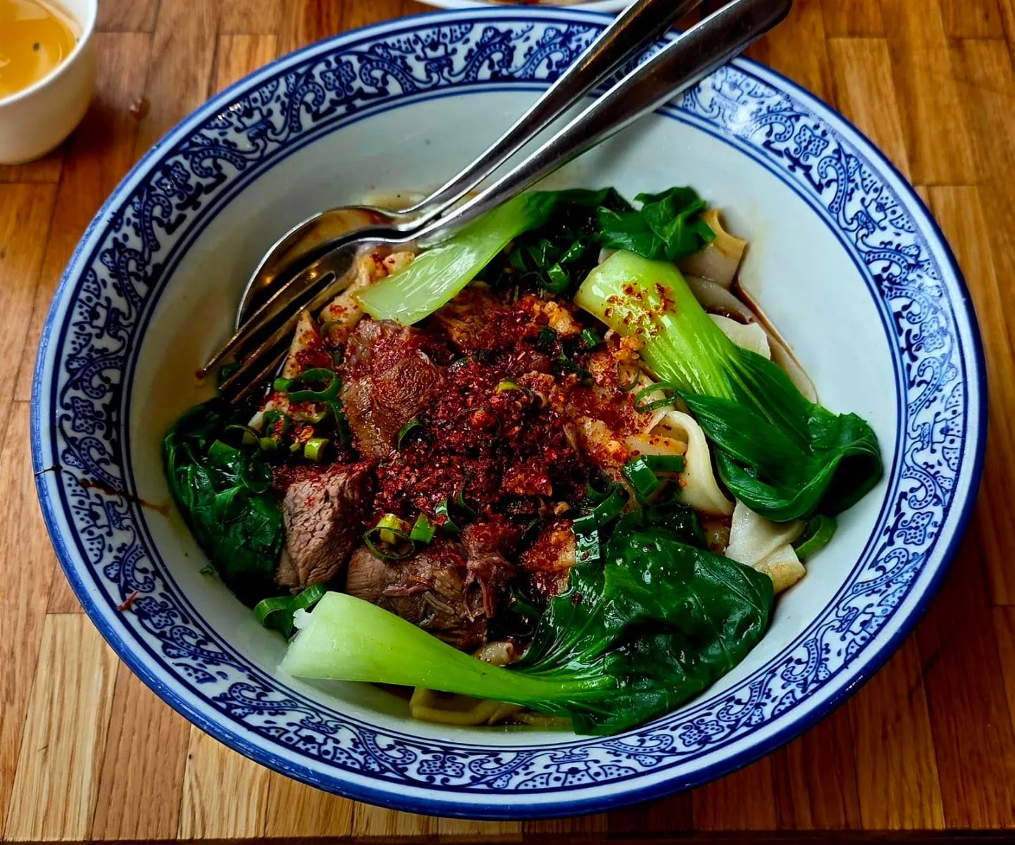 A bowl of wide, hand-pulled biang biang noodles with beef, bok choy and chilli flakes