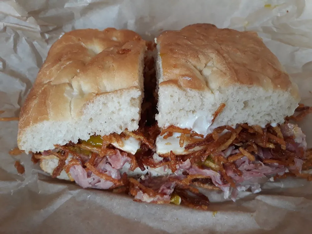 A sandwich in a soft split bun filled with ham, shoestring fries, pickles and a soft egg