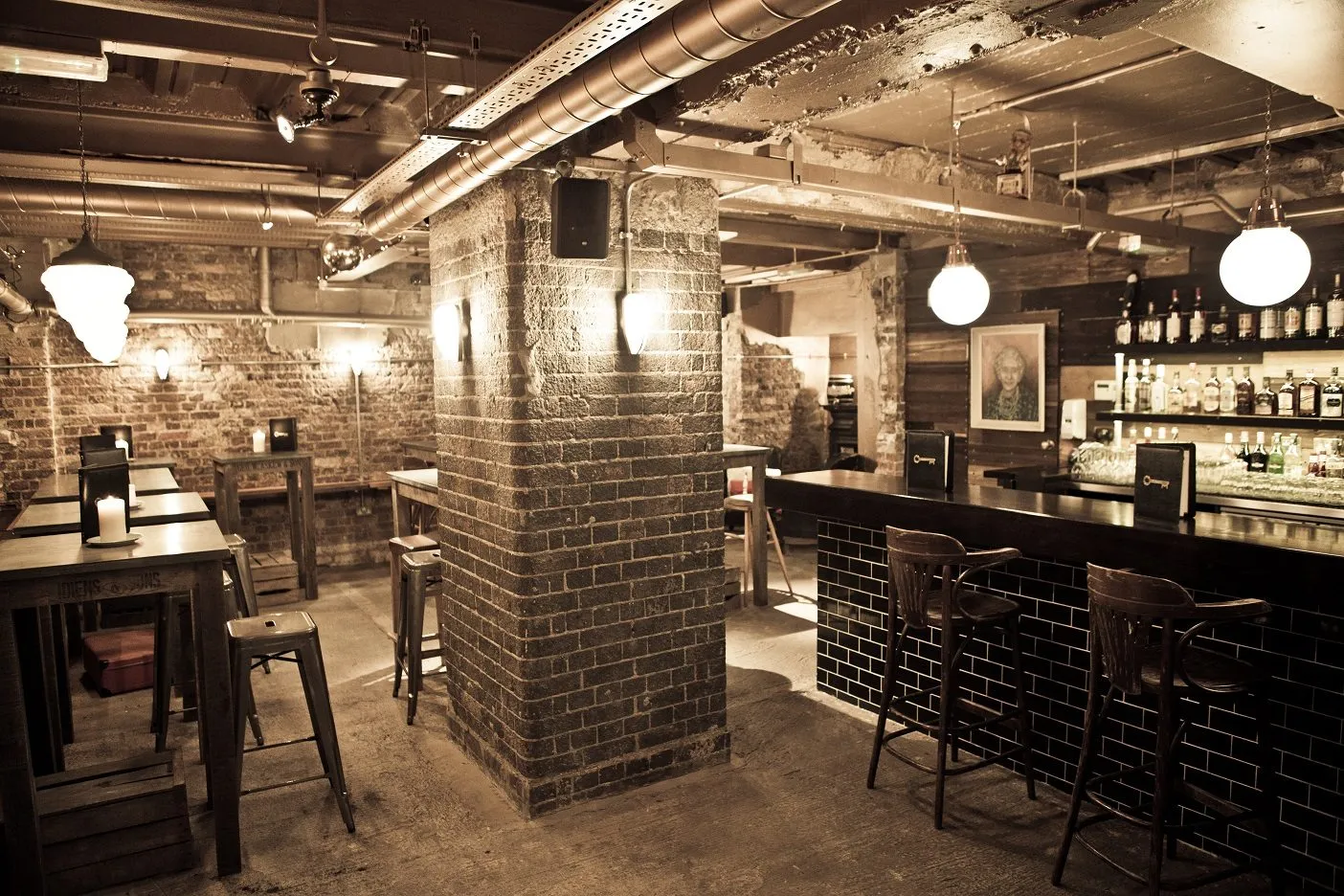 The basement bar at The Mayor of Scaredy Cat Town, with bare brick, exposed ducting, globe lights, a tiled bar front and candles on the tables