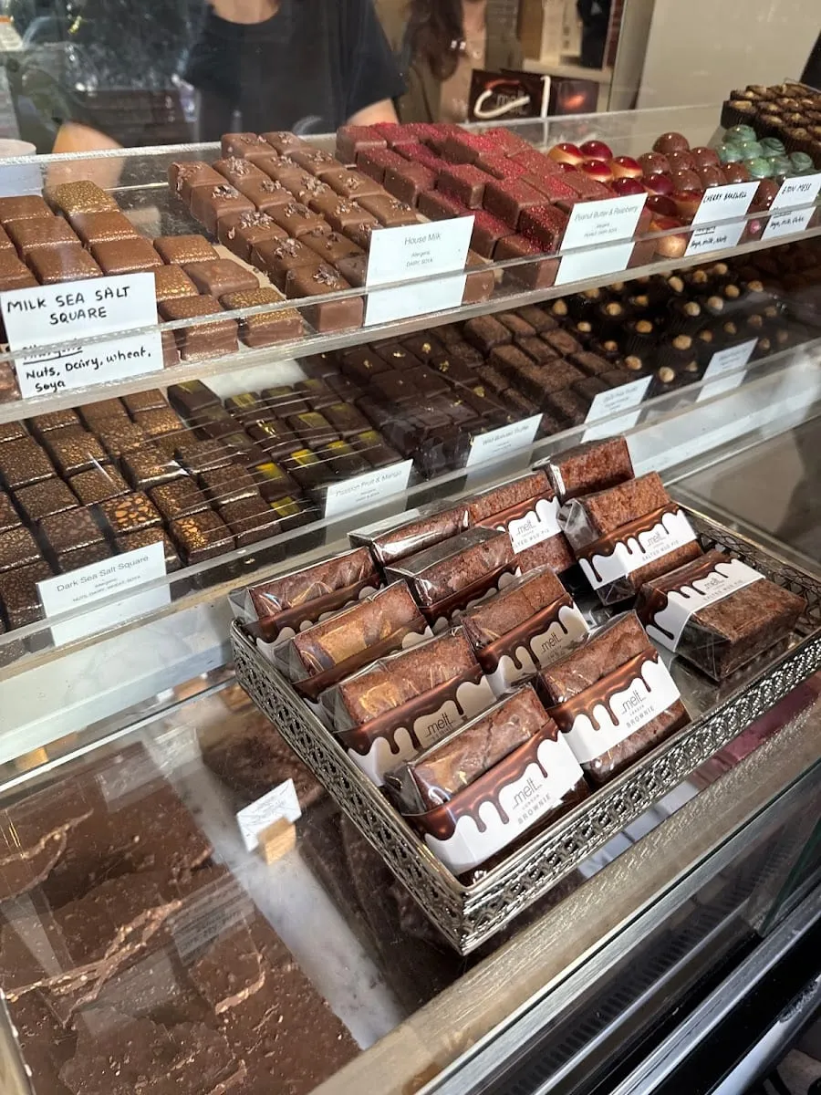 A glass display case of Melt's own chocolates — sea salt squares, fruit truffles and foil-wrapped brownies stacked in branded trays