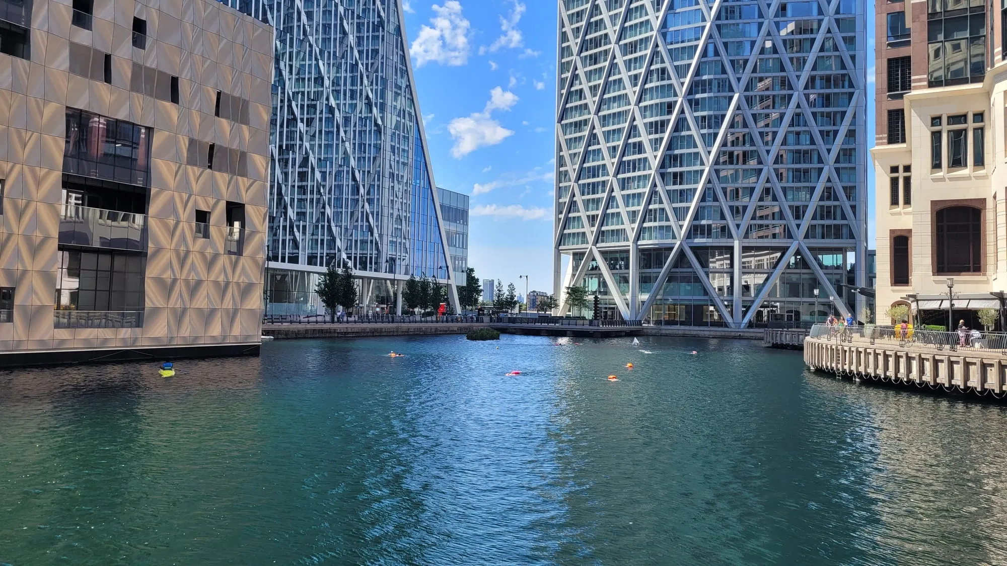 Swimmers with orange tow floats crossing the open water of Middle Dock between the towers at Canary Wharf