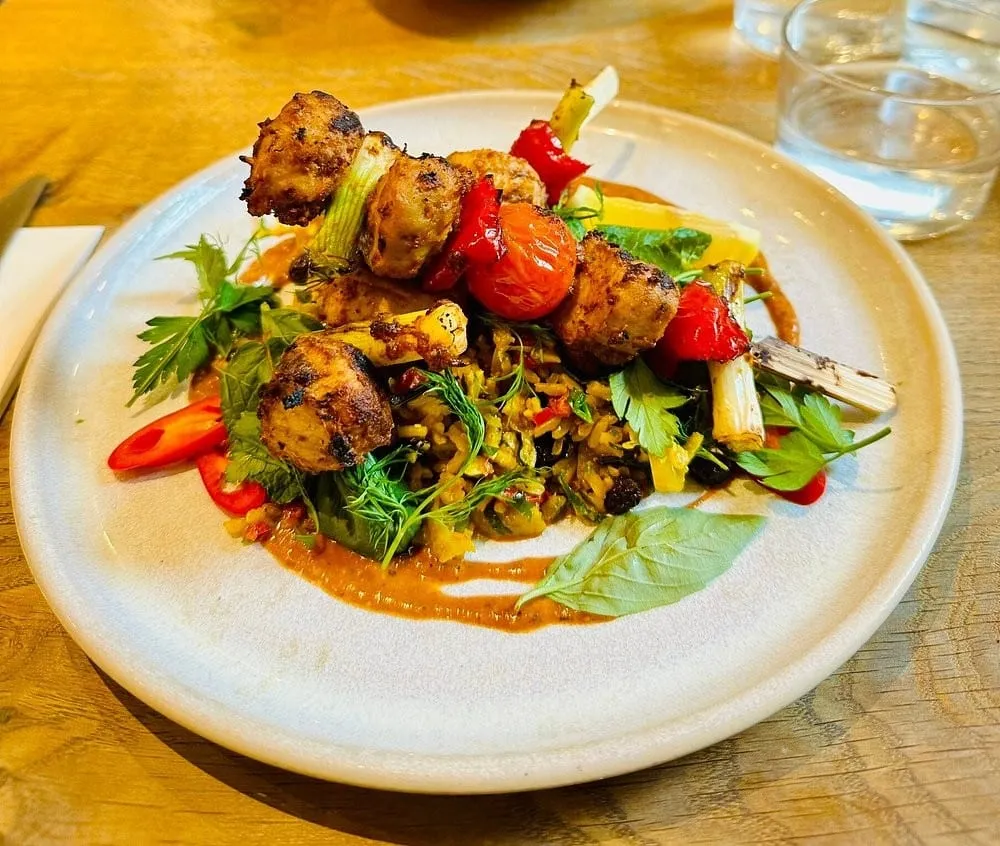 Skewers of browned, marinated pieces served over a herbed rice salad with charred tomatoes, chilli and a satay-style sauce on a pale plate