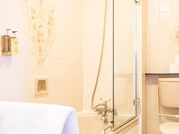 A cream-tiled bathroom at Mitre House Hotel with a bath, a hinged glass shower screen and a hand shower on a riser