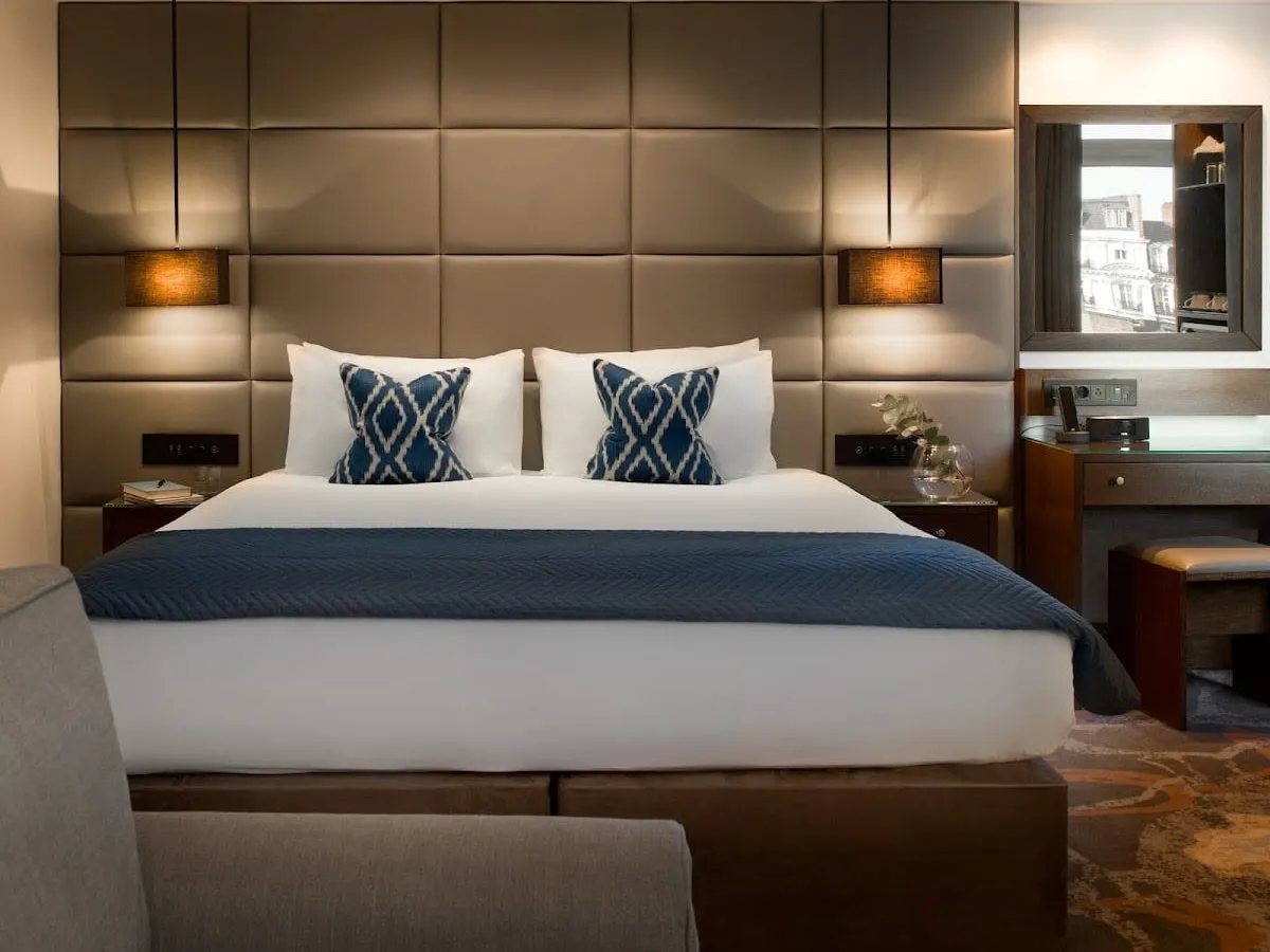 A double room at Montcalm Chilworth Townhouse with a wall of padded taupe leather panels behind the bed, navy ikat cushions, a navy throw and a mirror above a dark wood desk