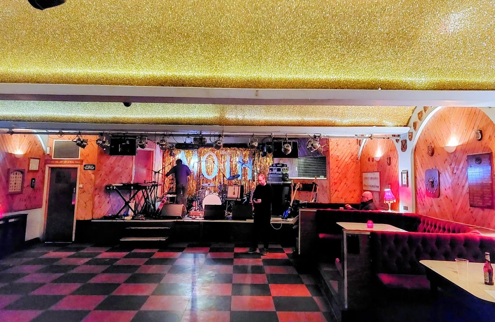 A stage at MOTH Club with a gold tinsel curtain spelling "MOTH", a glittery gold ceiling and a black-and-red checkerboard floor