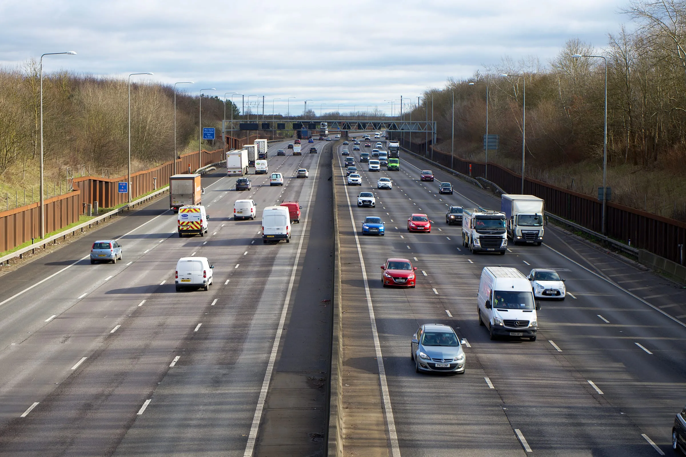Traffic running in both directions on a British motorway, cars and lorries in three lanes under a bright sky
